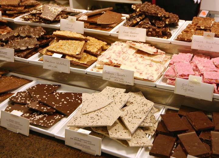 Nahaufnahme vom Vanille-, Erdbeer- und weiteren Schokotafeln, händisch und ungleich gebrochen