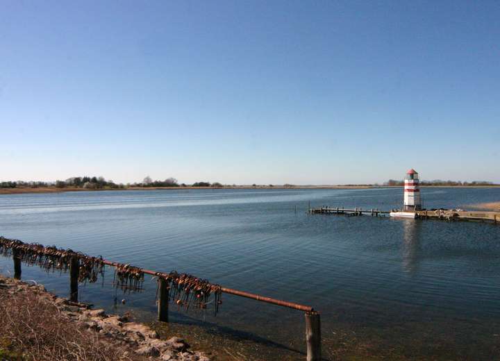 Sicht auf ein Brackgewässer mit rot-weiß-gestreiftem Leuchtturm und Fischernetzen 
