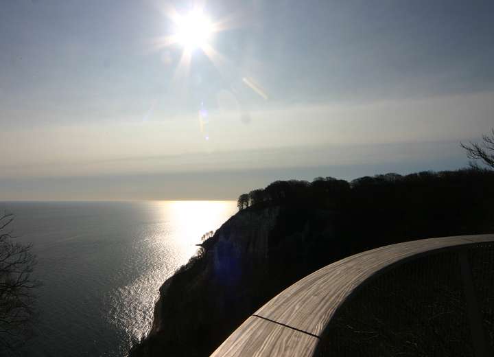 Blick auf das Meer mit gleißender Nachmittagssonne, man sieht den Bogen des Stubbenkammer Skywalks