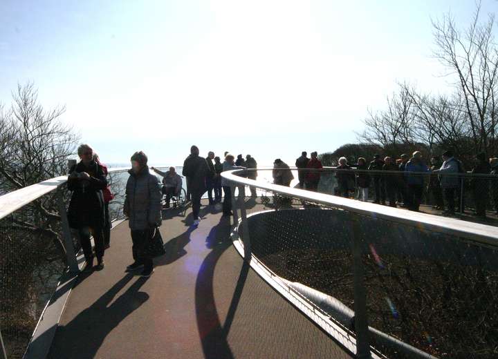 Reisegruppe schlendert den Boden des Stubbenkammer Skywalk entlang, der eine faszinierende Sicht auf Meer und Klippen gibt
